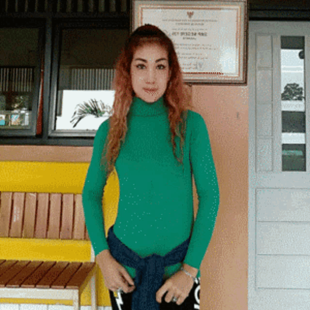a woman in a green turtleneck stands in front of a framed certificate