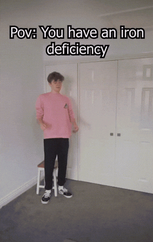 a man in a pink sweater and black pants is standing in a room with the words " you have an iron deficiency "