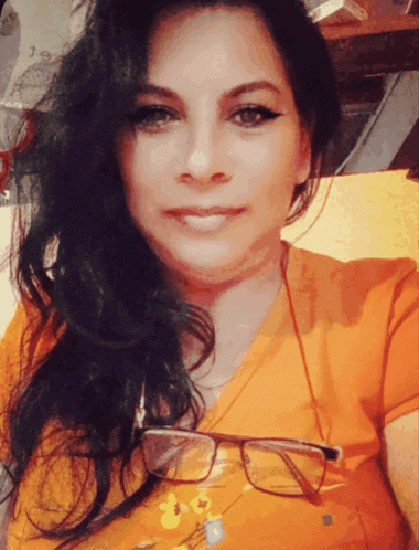 a woman wearing glasses and an orange shirt is smiling