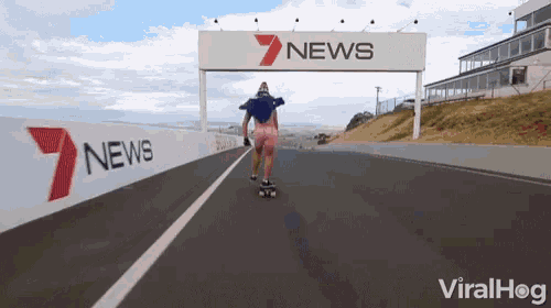 a person riding a skateboard on a road with a 7 news sign in the background