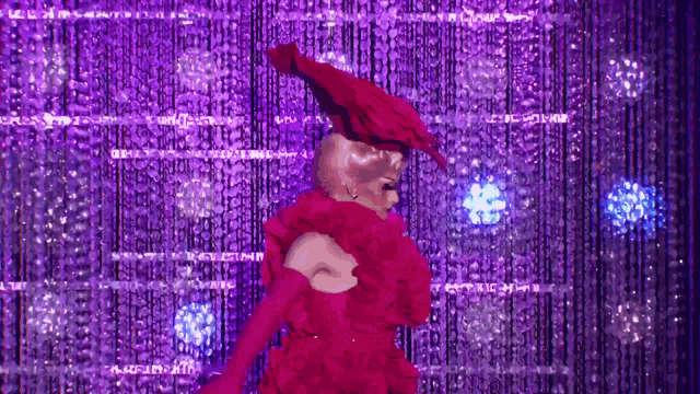 a drag queen is dancing on a stage wearing a red dress and a red hat .
