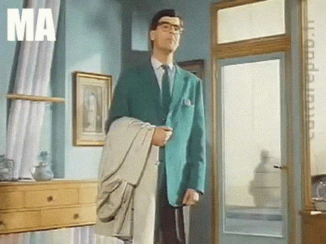 a man in a green suit and tie is standing in a room with the word ma on the bottom right