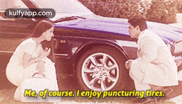 a man and a woman are kneeling next to a car and the woman is saying me of course i enjoy puncturing tires
