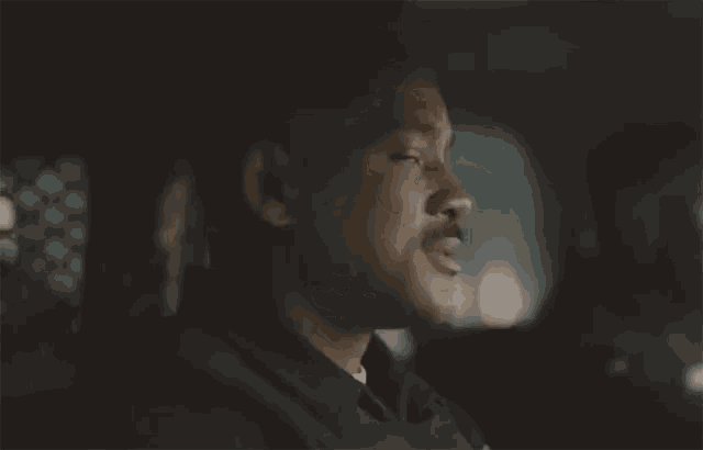 a man with a mustache is sitting in the back seat of a car and looking at the camera .