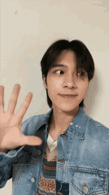 a young man wearing a denim jacket waves his hand