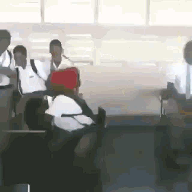 a group of people are standing in a room and one of them has a red bag