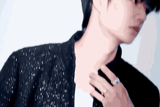 a man wearing a black jacket and a ring on his finger is adjusting his tie .