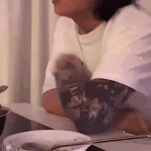 a person with a tattoo on their arm is sitting at a table with a bowl of food .