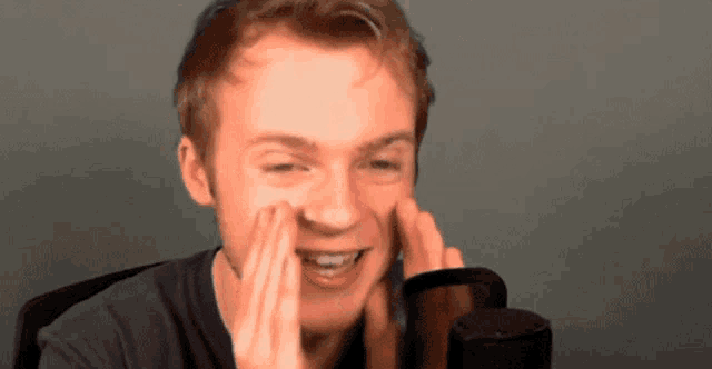 a young man wipes his face in front of a black microphone