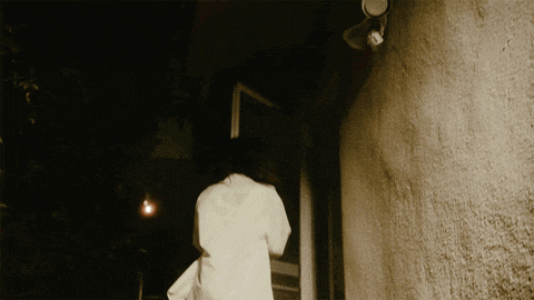 a woman in a white shirt is walking down a hallway at night