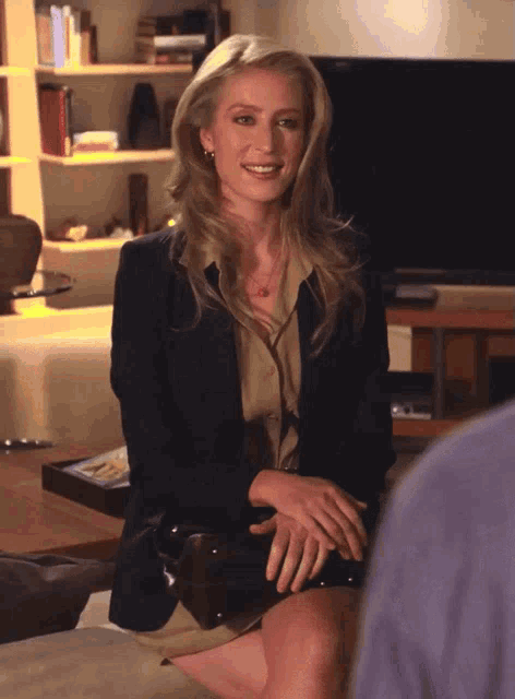a woman in a black jacket sits in front of a sony television