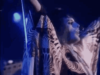 a man is singing into a microphone on a stage while wearing a zebra print dress .