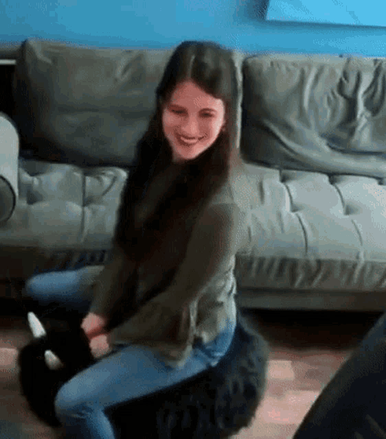 a woman is sitting on the floor next to a couch with a black cat .
