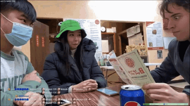 a man wearing a mask looks at a menu while a woman wearing a green frog hat looks on
