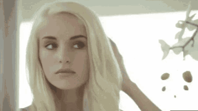 a woman with blonde hair and blue eyes is looking at herself in the mirror .
