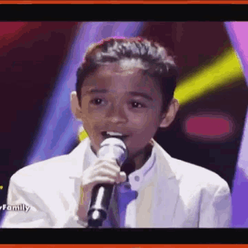 a young boy in a suit is singing into a microphone