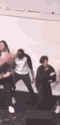 a group of people are dancing on a stage in front of a white wall .