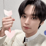 a young man in a suit and tie is holding a pink heart and arrow .