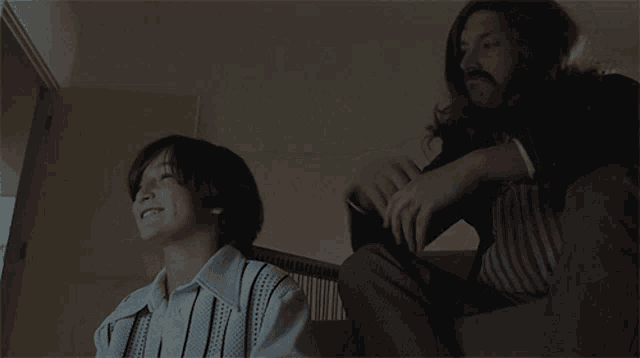 a man with long hair is sitting next to a young boy