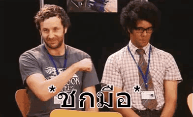 two men are sitting next to each other and one of them is pointing at the camera in a language other than english .