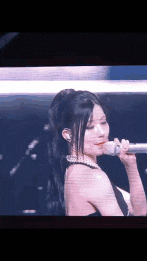 a woman in a black dress is singing into a microphone