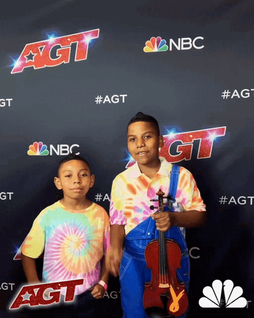 two young boys standing in front of a sign that says agt on it