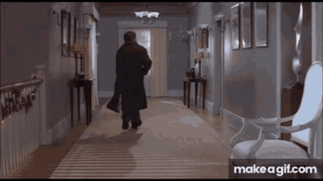 a man in a black coat is running down a hallway