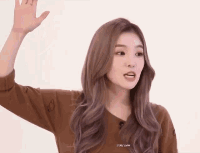a woman in a brown sweater is waving her hand .
