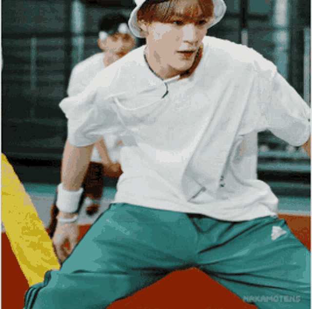 a young man wearing a white shirt and green pants is standing on a red surface .