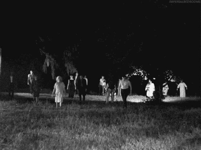 a black and white photo of a group of zombies walking in a field at night .