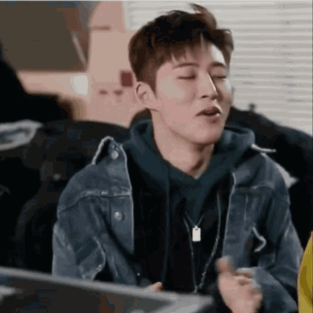 a young man wearing a denim jacket and a green hoodie is making a funny face