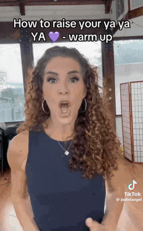 a woman with curly hair is making a funny face while wearing a black tank top .