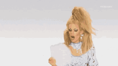 a drag queen is holding a piece of paper in her hand and screaming .