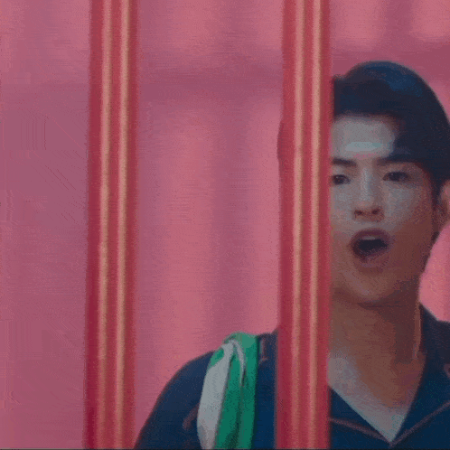 a man in a blue shirt is peeking out from behind a fence .