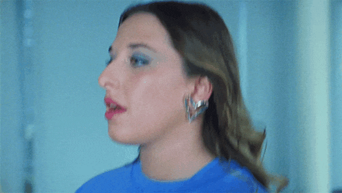 a woman wearing a blue shirt and earrings looks to the side