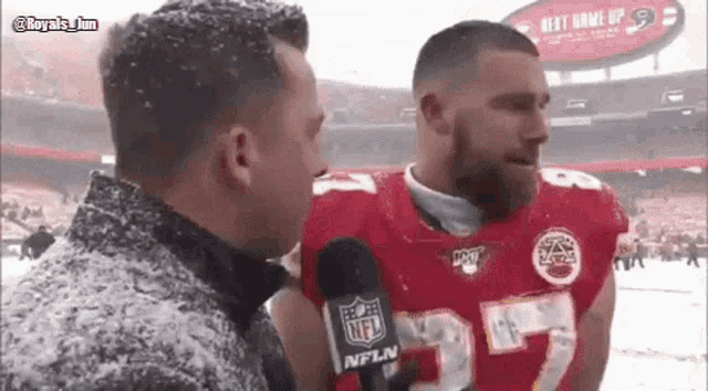 a man in a nfl jersey is talking to another man in a snowy stadium