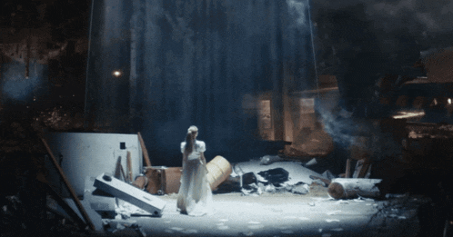 a woman in a white dress is standing in a destroyed area