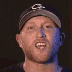 a man with a beard is wearing a baseball cap and making a face .