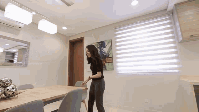 a woman is standing in a dining room with a table and chairs .