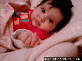 a baby in a red shirt is laying on a bed with a blanket .