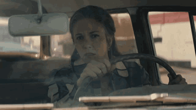 a woman sits in a car with her hand on the steering wheel looking out the window