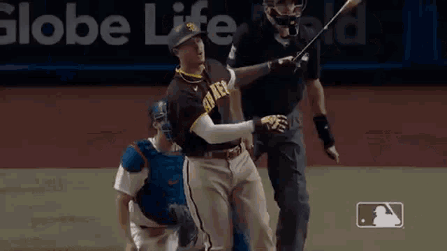 a baseball player is swinging a bat at a ball while a catcher looks on .