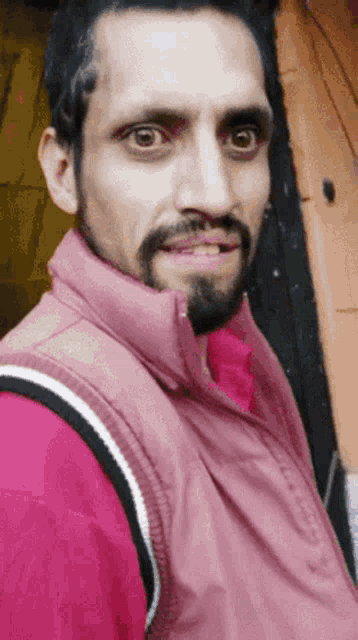 a man with a beard wears a pink vest and a red shirt