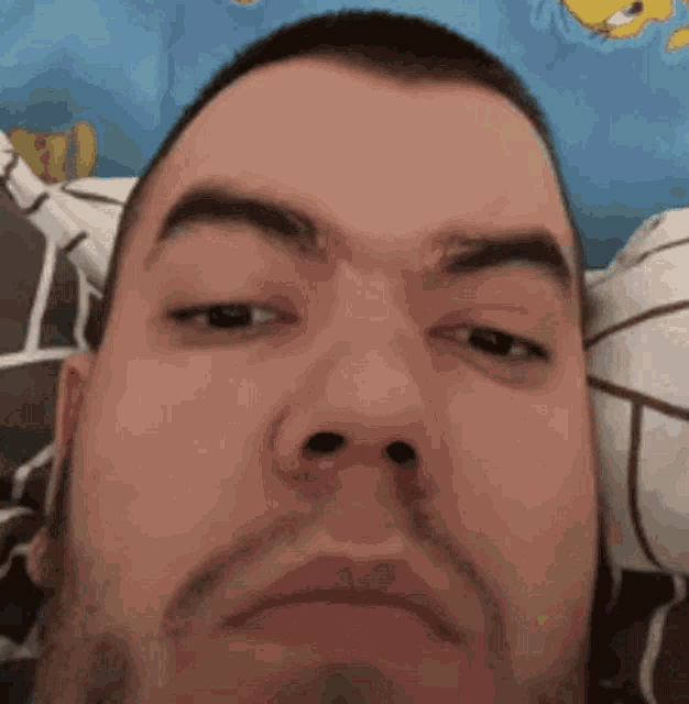 a man with a beard is laying in bed and making a funny face with his eyes closed .