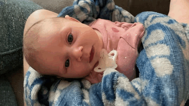 a baby with a pacifier in its mouth is laying on a blue blanket