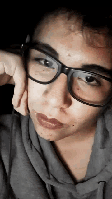 a woman wearing glasses and a gray hoodie looks at the camera
