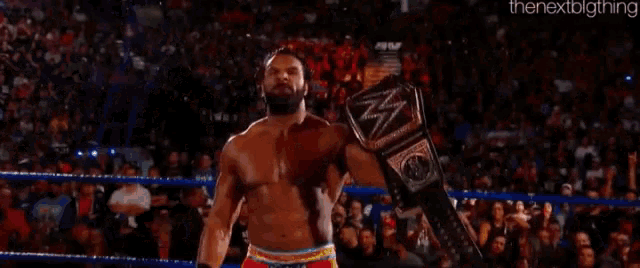 a shirtless wrestler is holding a wrestling championship belt in front of a crowd .
