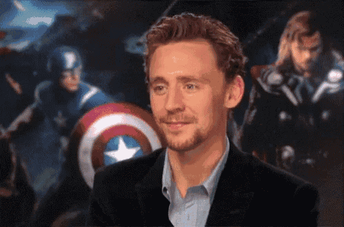 a man in a suit is smiling in front of a poster of captain america