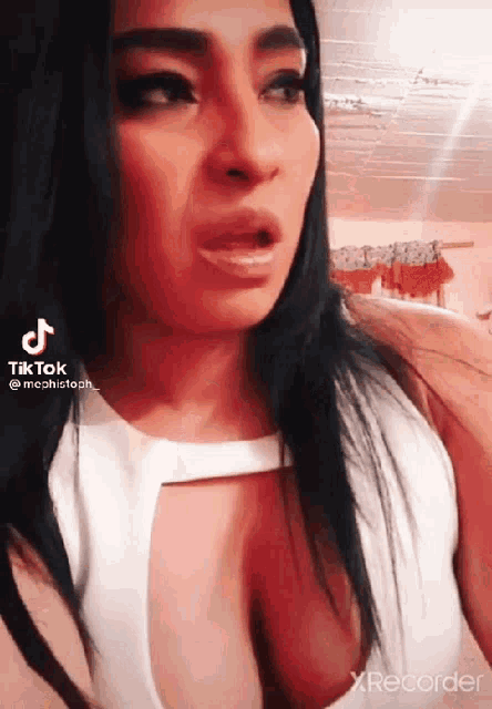 a woman in a white top with a plunging neckline is making a face .