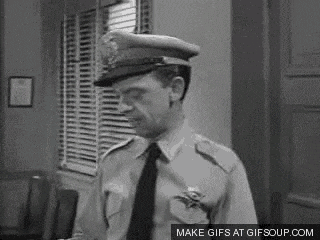 a black and white photo of a man in a police uniform and tie standing in a room .